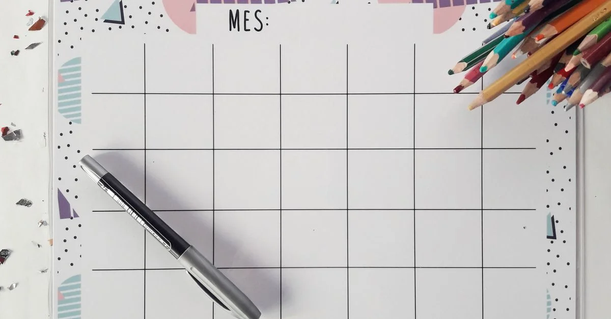 Vue de dessus d'un agenda mensuel avec un stylo et des crayons de couleur, parfait pour organiser votre emploi du temps.