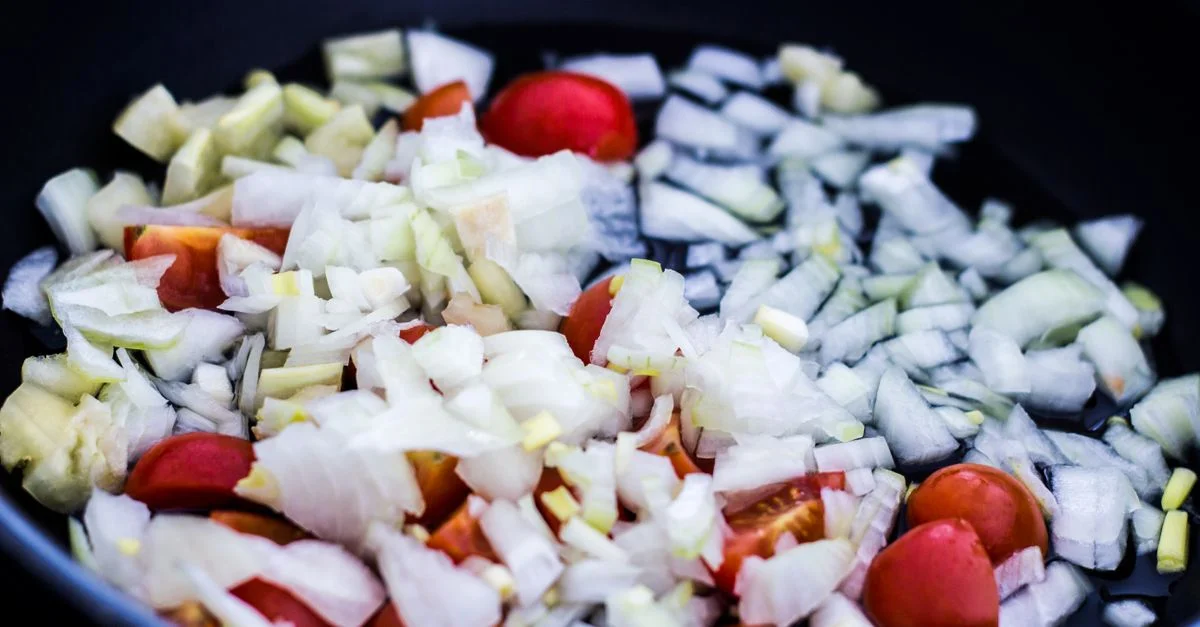 Gros plan sur des oignons hachés et des tomates cerises dans une poêle, parfait pour des thèmes culinaires.