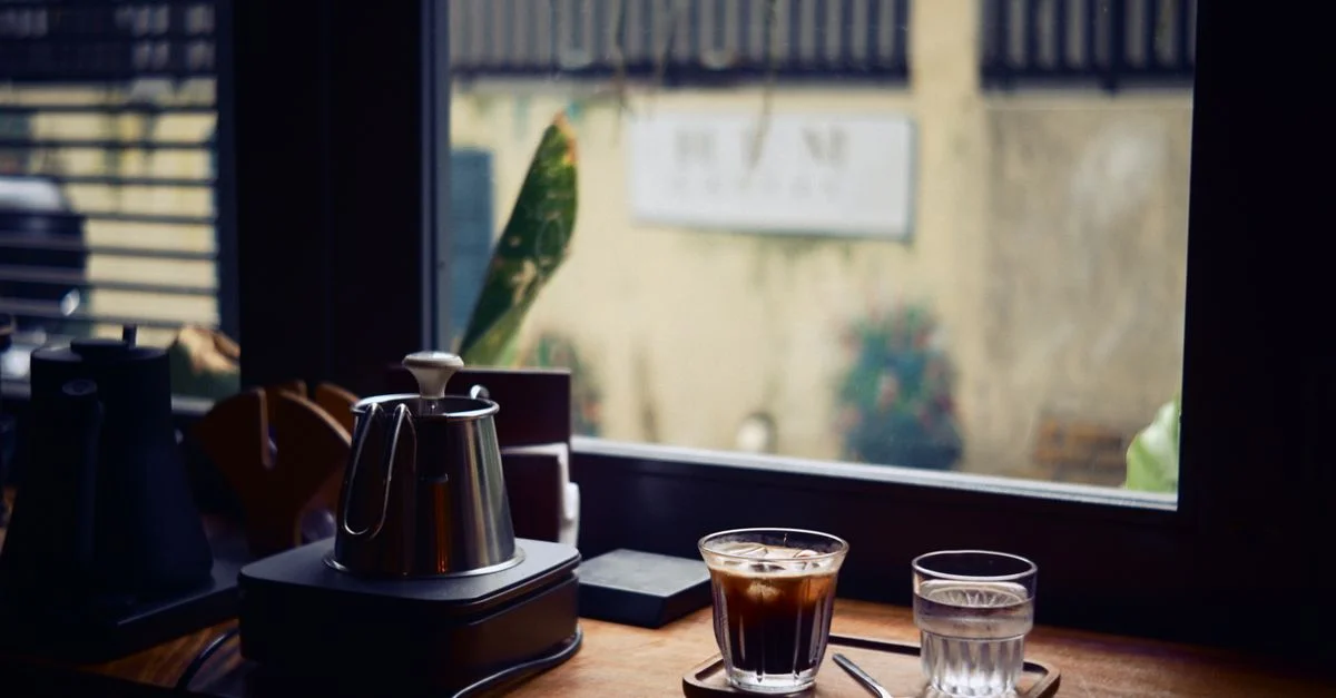 Une scène de café intérieur chaleureuse, avec un café et de l'eau sur une table en bois près de la fenêtre.