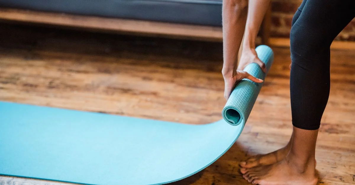 Gros plan sur une femme en train de rouler un tapis de yoga sur un sol en bois dans un cadre de studio à domicile.