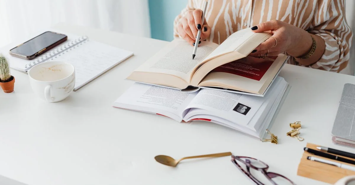 Femme lisant et prenant des notes à un bureau avec des livres, un carnet et du café