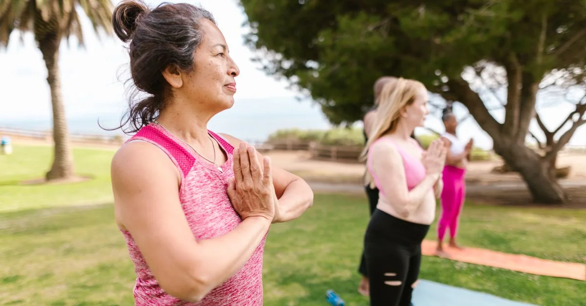 Une femme senior pratiquant le yoga en groupe dans un parc ensoleillé, promouvant la santé et la relaxation.