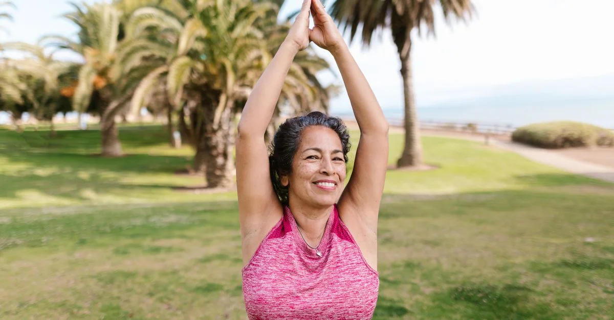 Femme âgée appréciant le yoga dans un parc ensoleillé, mettant en avant un vieillissement positif et le bien-être.