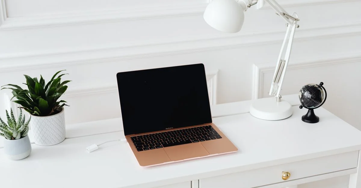 Espace de travail propre et élégant avec un ordinateur portable, un lampadaire et des plantes en pot sur un bureau blanc.