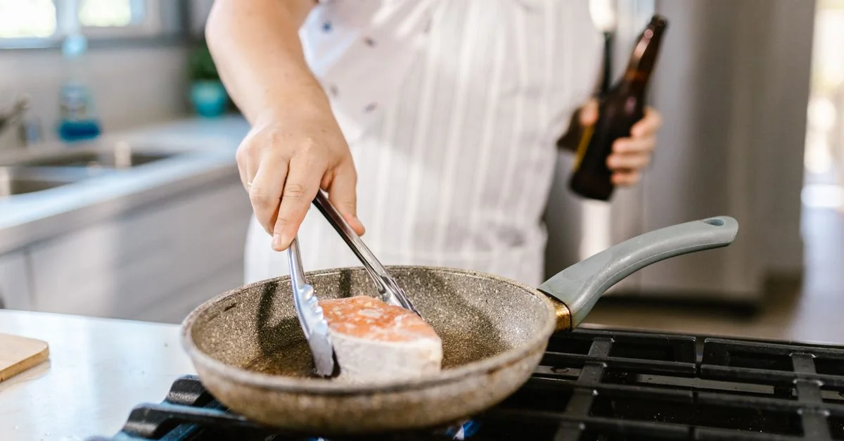 Une personne cuisinant un filet de saumon dans une poêle sur une cuisinière.