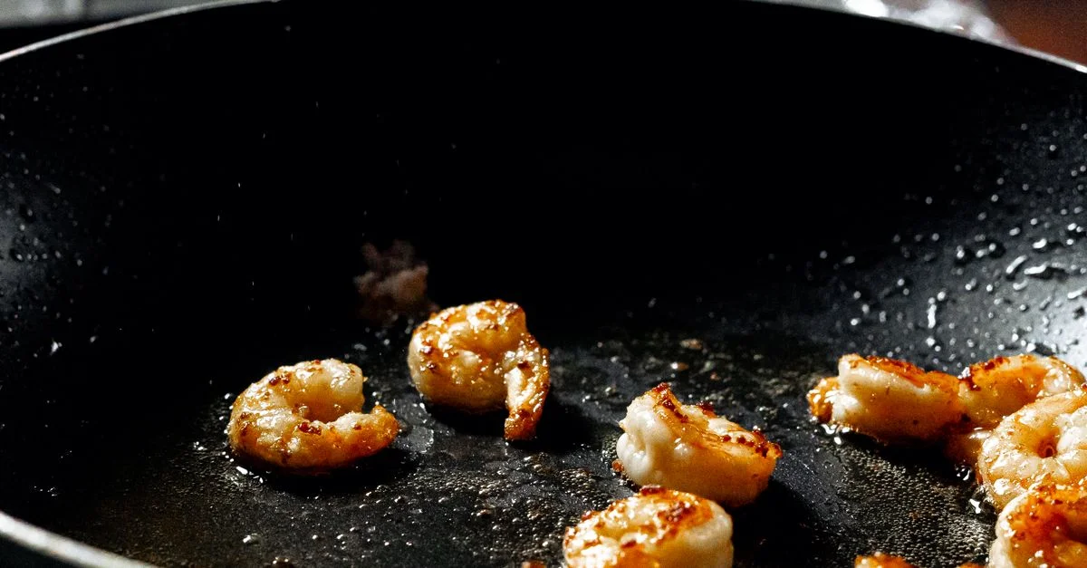Gros plan sur des crevettes parfaitement saisies dans une poêle mettant en avant les compétences culinaires.